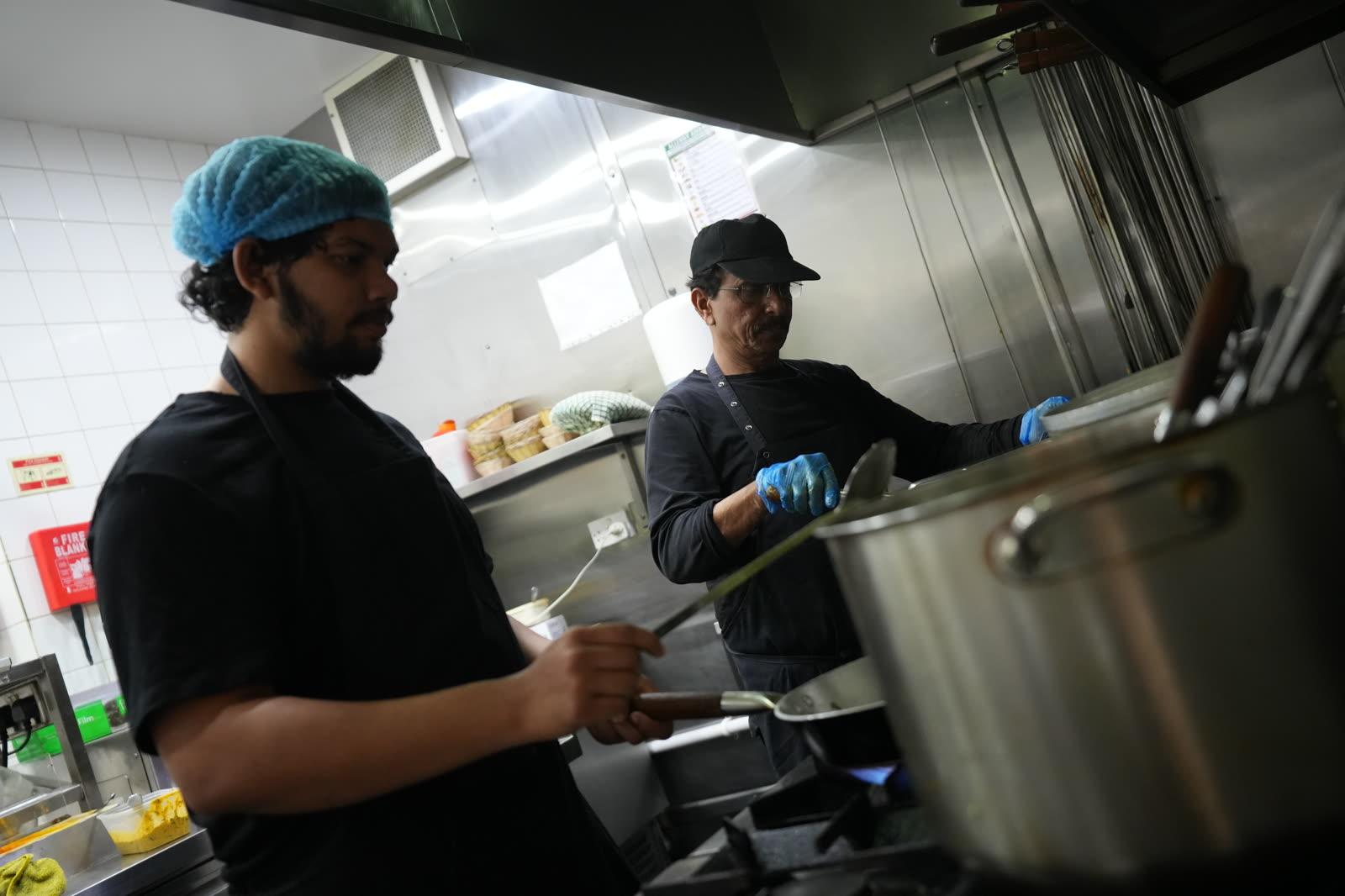 A chef ladling curry from a large pot, steam rising over the curry station