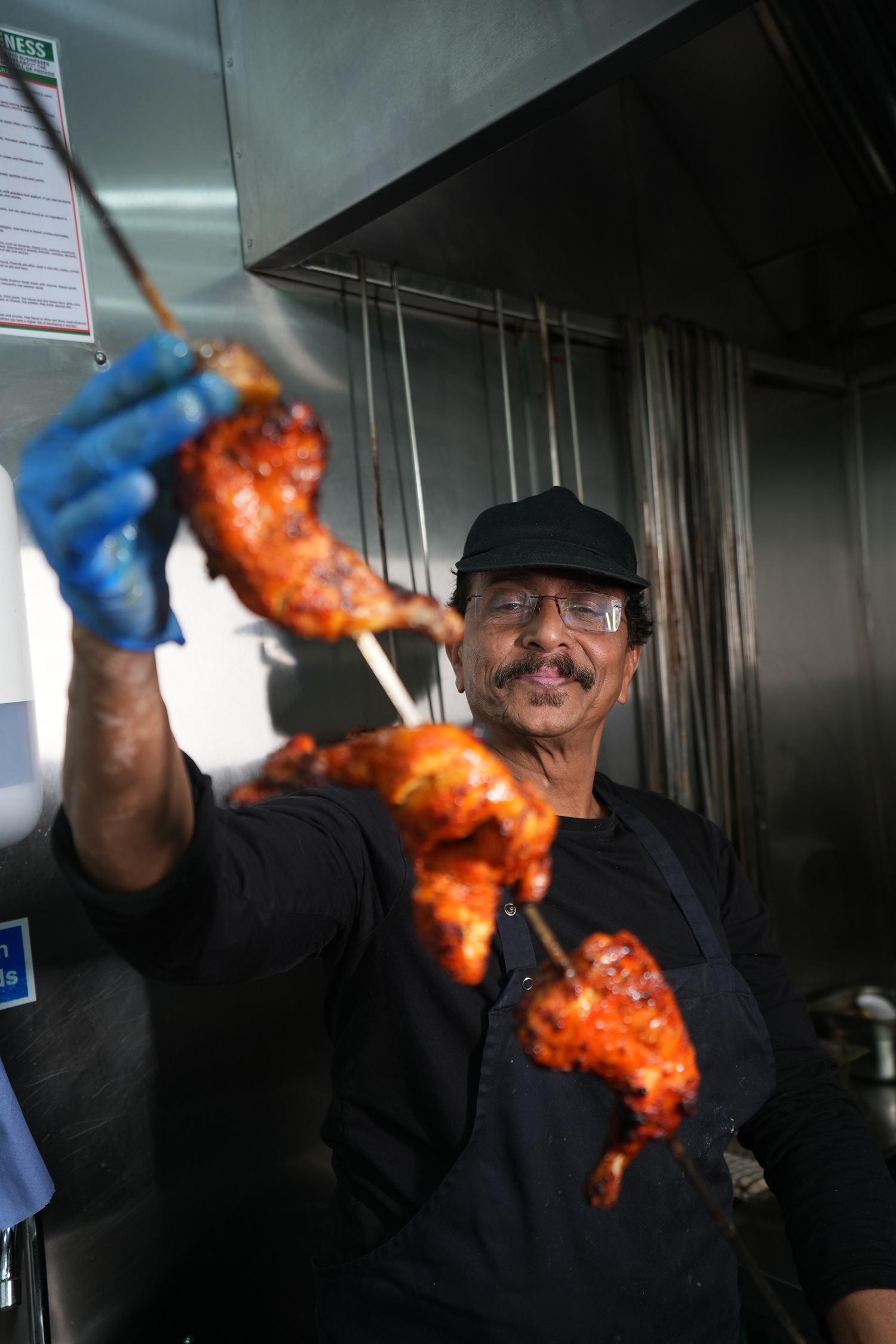 The chef smiling as he pulls sizzling skewers from the tandoor